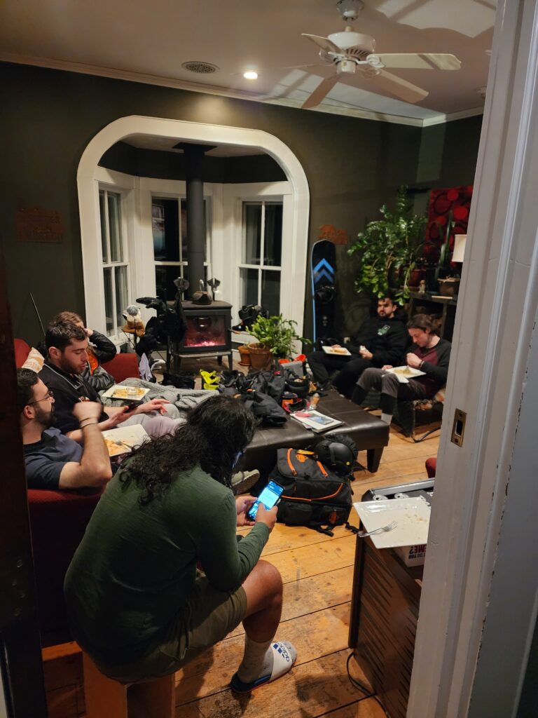 A group of guests enjoying a meal in the common room, warmed by a fire crackling in the wood stove.